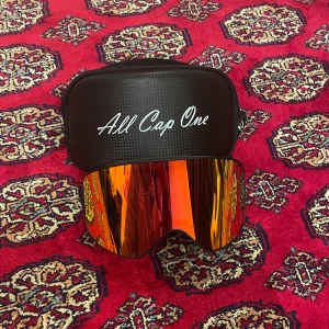 Skidglasögon från All Cap One - Snygga skidglasögon med röd spegelglas från All Cap One. De har en bred, justerbar rem med logotyp och kommer i ett praktiskt fodral. Perfekta för vintersport och skyddar mot starkt solljus. Helt nya aldrig användna, otroligt snygga och slutsålda på deras hemsida!                                     Vid frågor och funderingar hör gärna av er🤗                                        Mvh Doré.reselll