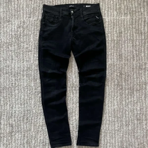 Replay jeans anbass  - Snygga svarta Replay Anbass jeans med en slim passform. De har en klassisk femficksdesign och stängs med dragkedja och knapp. Perfekta för en stilren look.