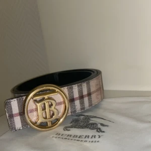 Rutig bälte från Burberry - Snyggt bälte från Burberry med klassiskt rutigt mönster och en elegant guldspänne med logotyp. Perfekt för att ge en lyxig touch till din outfit. Bältet har en stilren design och är tillverkat i högkvalitativt material.