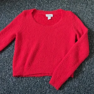 Röd stickad tröja från Monki - Säljer en snygg röd stickad tröja från Monki. Tröjan har en rund halsringning och långa ärmar. Perfekt för att hålla sig varm och stilren under kyligare dagar. Har ett litet hål på nedre kanten som inte syns. 