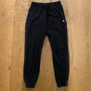 Svarta mjukisbyxor från Champion - Säljer ett par svarta mjukisbyxor från Champion i storlek XS. Byxorna har elastisk midja med snörning och ribbade muddar vid bensluten. Champion-loggan finns både på framsidan och längs benet.