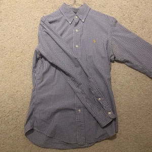 Ralph Lauren skjorta - Snygg blårutig skjorta från Ralph Lauren i storlek S. Skjortan har långa ärmar och en klassisk krage med knappar. Den är broderad med Ralph Laurens ikoniska logga i gult på bröstet. Perfekt för en stilren look!