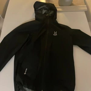 Svart regnjacka från Haglöfs - Säljer en svart regnjacka från Haglöfs i storlek S. Jackan har en praktisk huva och dragkedja framtill. Perfekt för regniga dagar och utomhusaktiviteter. Det är goretex vilket gör den bättre mot vind och regn. Mycket bra skick. Använd cirka 5 gånger. Skick 9,5/10