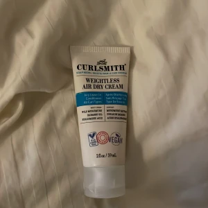 Curlsmith Weightless Air Dry Cream - En lätt leave-in conditioner för alla locktyper från Curlsmith. Innehåller vild solrosfröolja och druvkärnolja för att ge näring och mjukhet utan att tynga ner håret. Vegansk och fri från sulfater och silikoner. Perfekt för att definiera och återfukta lockar.