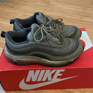 Nike Air Max 97 i olivgrön - Snygga Nike Air Max 97 sneakers i en olivgrön färg. Skorna har en ikonisk vågig design med synlig Air-enhet i sulan för extra komfort. Perfekta för en stilren look.