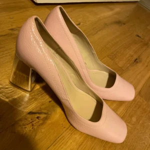 Rosa klackar från Zara - Säljer ett par eleganta rosa pumps från Zara med en fyrkantig tå och hög klack. Skorna har en glansig yta och är perfekta för att ge en stilren touch till din outfit. Aldrig använt de