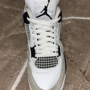 Jordan 4 Black military - Snygga Jordan 4 black military i vitt och svart med klassisk Jumpman-logga. Skorna har snörning och en stilren design med meshdetaljer och kontrasterande svarta inslag.