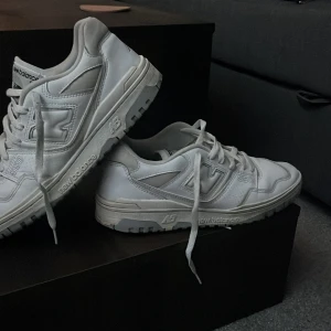 Vita New Balance 550 sneakers - Säljer ett par vita New Balance 550 sneakers. Skorna har en klassisk design med snörning och är tillverkade i syntetmaterial. Perfekta för en stilren look.Ett litet slit hål i hälen på vänstra skon annars väldigt bra kvalite!