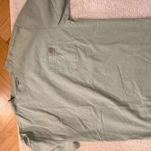 Grön t-shirt med bröstficka - Snygg grön t-shirt med en praktisk bröstficka. Perfekt för en avslappnad stil. Kortärmad och tillverkad i ett mjukt material. Från dickies. Storlek M. Mycket bra skick.