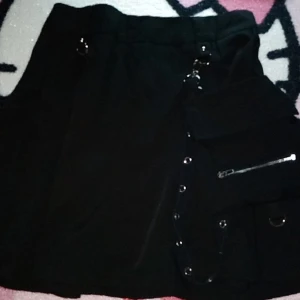 Snygg svart kjol - Snygg svart kjol med coola detaljer som dragkedja, ringar och liten väska som man kan ta bort. Size medium med bra funkande dragkedja. Oanvänd sen 2021.