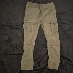 Olivgröna cargopants med snörning - Säljer ett par olivgröna cargopants med elastisk midja och snörning. Byxorna har flera praktiska fickor på sidorna och en avslappnad passform. Perfekta för en casual look.