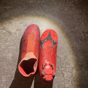 Röda fotbollsskor från Nike - Snygga röda fotbollsskor från Nike med en strömlinjeformad design och svarta detaljer. Skorna har en tight passform och är perfekta för snabba rörelser på planen.