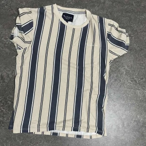 Randig t-shirt från French Connection - Snygg randig t-shirt från French Connection i beige och blått. Perfekt för en avslappnad stil. Kortärmad med rund halsringning.