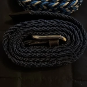 Färgglada flätade bälten - Säljer ett set av fyra flätade bälten i olika färger. Ett blått och vitt, ett beige, ett svart och ett mörkblått. Alla bälten har en stilren metallspänne och är perfekta för att ge en färgklick till din outfit.