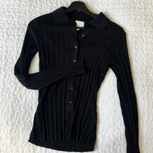 Svart ribbad kofta - Snygg svart ribbad kofta med knappar framtill. Den har långa ärmar och en klassisk krage, perfekt för en stilren look.
