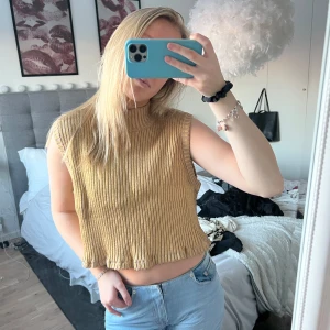 Beige ribbad ärmlös topp - Säljer en snygg beige ribbad topp med hög hals och ärmlös design. Toppen är croppad och har en avslappnad passform, perfekt för en trendig look. Passar mig som är en S!