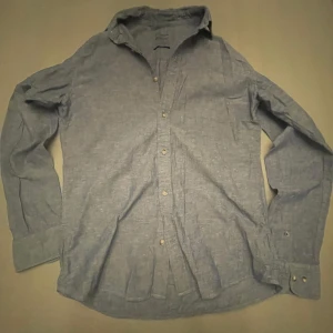 Blå skjorta från Essentials - Snygg blå skjorta från Essentials med regular collar. Perfekt för sommaren med sin lätta design. Skjortan har långa ärmar och knappar framtill. Inget pris är spikat i sten!