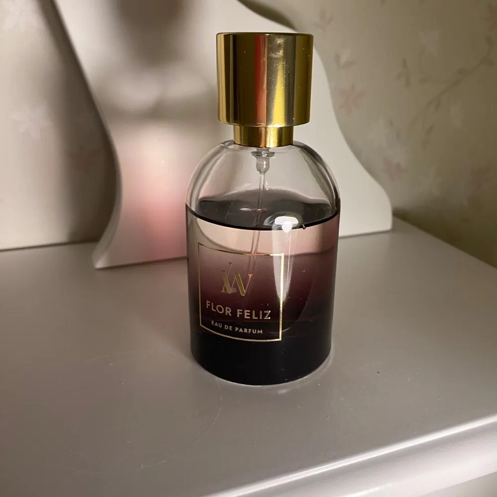 Flor Feliz Eau de Parfum från märket W. Flaskan har en elegant design med en gradient från mörk till ljus färg och en gyllene kork. Tillverkad i Frankrike, denna parfym erbjuder en lyxig doftupplevelse.. Perfume.