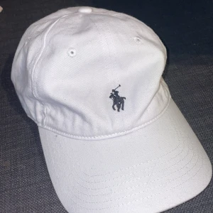 Vit keps från Ralph Lauren - Snygg vit keps från Ralph Lauren med det klassiska broderade logotypen framtill. Perfekt för en stilren look. Säljer den helt oanvänd