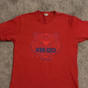 Röd t-shirt från Kenzo Paris - Säljer en röd t-shirt från Kenzo med ett coolt tigertryck i blått och rött på framsidan. T-shirten är kortärmad och har en rund halsringning. Perfekt för en avslappnad stil. Storlek xl men sitter som L