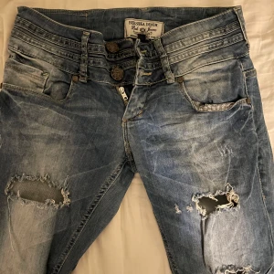 Low waist jeans med slitningar från Bershka - Snygga blå jeans från Bershka med slitningar på låren och knäna. Köpta på en marknad i spanien men har inga täcken på användning De har en låg midja och en tight passform som framhäver figuren. Skulle tro att dom är väldigt lätta att sy om till utsvängda och dom har väldigt coola detaljer. Skriv vid frågor💕