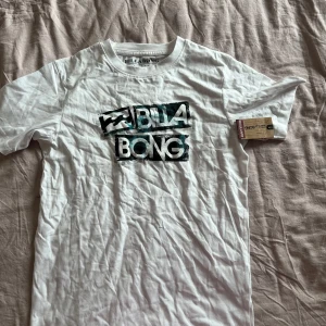 Vit t-shirt från Billabong - Säljer en snygg vit t-shirt från Billabong med ett coolt tryck i svart och blått på framsidan. Perfekt för en avslappnad stil och passar till det mesta. T-shirten är i nyskick och har korta ärmar.
