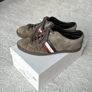 Moncler skor (Box medföljer) - Skor i mocka från Moncler i storlek 43. Box medföljer. Varsamt använda. Bra skick. Däremot defekt på sulan, men inget man märker av när man har på sig skorna.