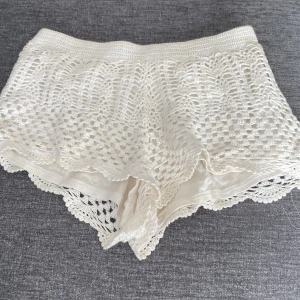 Vita virkade shorts - Säljer ett par supergulliga vita virkade shorts. De är perfekta för sommaren med sitt luftiga och bekväma material. Shortsen har en elastisk midja och ett fint spetsmönster som ger en romantisk touch. Perfekta för en dag på stranden eller en somrig utflykt! 🌞