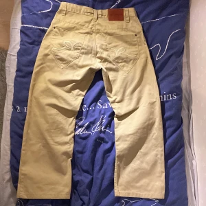 Beige byxor från Rocawear - Säljer ett par snygga beige byxor från Rocawear🔥De har en loose passform och är perfekta för både vardag och fest. Byxorna har en cool broderad detalj på bakfickorna. Materialet känns slitstarkt och bekvämt! Ganska korta i längden