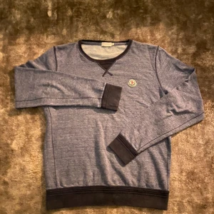 Blå tröja från Moncler - Säljer en snygg blå tröja från Moncler i storlek M. Tröjan har långa ärmar och en liten Moncler-logga på bröstet. Den är perfekt för både vardag och lite kyligare dagar. Muddar i mörkare nyans vid ärmslut och nederkant. Va inte rädd för att skriva😁👍
