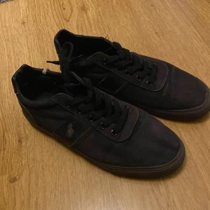 Svarta sneakers från Ralph Lauren - Säljer ett par svarta sneakers från Ralph Lauren. De har en klassisk design med snörning och är i välanvänt skick. Perfekta för vardagsbruk och passar till det mesta. Skorna har en diskret logga på sidan och är bekväma att gå i.
