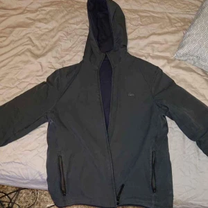 Svart jacka med huva - Tvåsidig Lacoste (limited edition) jacka perfekt för vår/höst, jackan har då två sidor ena sidan är grå och andra sidan mörkblå den är i storlek XS men passar perfekt för S och även M (så länge du inte har för långa armar). Den är i mycket bra skick.