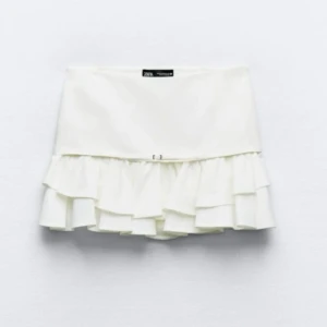 Vit volangkjol från Zara - Säljer en superfin vit volangkjol från Zara. Den är kort och har flera lager av volanger som ger en söt och lekfull look. Perfekt för sommardagar eller en festlig kväll! 🕺