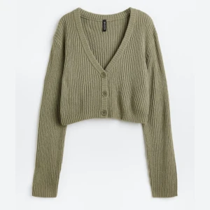 Olivgrön ribbad kofta - Säljer en superfin olivgrön ribbad kofta med en croppad stil. Den har en v-ringad design och knappar framtill. Perfekt för höst och vår när du vill ha något mysigt men ändå stilrent. Passar perfekt till både jeans och kjol! Nypris 180kr💚