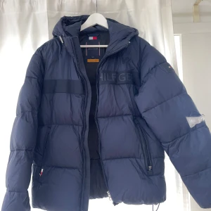 Tommy Hilfiger vinterjacka mörkblå - Säljer denna snygga men tyvärr skadade vinterjacka från Tommy Hilfiger       Skick: 10/10 förutom skadan på ärmen, använd 1 gång då en klasskamrat förstörde den, går att täcka över dock Nypris: 2500kr Pris går att förhandla  Kontakta för fl