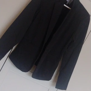 Svart kavaj från ICHI - Säljer en stilren svart kavaj från ICHI i storlek L. Perfekt för både vardag och fest! Kavajen har en klassisk design med långa ärmar och en snygg passform. Den är tillverkad i ett bekvämt material som gör den lätt att bära hela dagen.