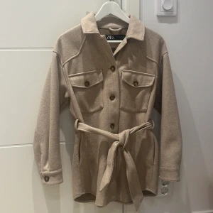 Zara jacka  - Zara jacka i färgen brun/camel. Med ett bälte i midjan. Jackan är i storlek xs
