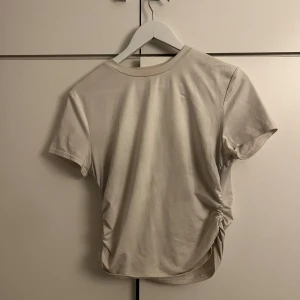 Beige kortärmad t-shirt - Säljer en vit T-shirt  i bomull. Den har en unik detalj med rynkning på sidan som ger en snygg twist.!