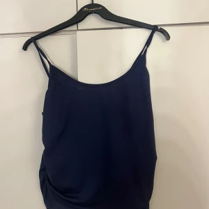Mörkblå linnetopp - Säljer en stilren mörkblå linnetopp med smala axelband. Perfekt för sommardagar eller som ett lager under en kavaj. Toppen är i ett mjukt och lätt material. En liten fläck vid kanten därav priset 