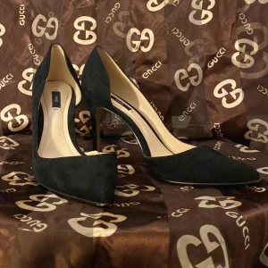 Svarta klackskor från MNG - Snygga svarta klackskor från MNG i mocka. De har en elegant spetsig tå och hög klack, perfekt för festliga tillfällen. Skorna är i bra skick och ger en stilren look. Passar perfekt till både klänning och byxor.