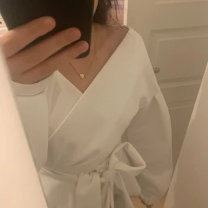 Vit omlottklänning med knytband - Säljer en superfin vit omlottblus med knytband i midjan. Blusen har långa ärmar och en elegant v-ringad design. Perfekt för vår och sommar, både till vardags och festliga tillfällen. Den är i nyskick och redo för nya äventyr!