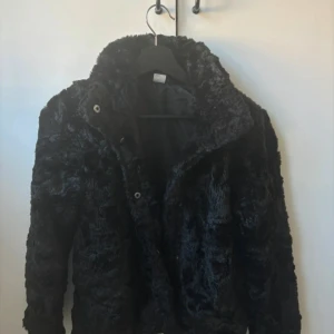 Svart pälsjacka - Säljer en supermjuk och fluffig svart pälsjacka. Perfekt för kalla vinterdagar och höstkvällar. Jackan har långa ärmar och stängs med knappar framtill. Den är i bra skick och passar både till vardags och fest. Ett måste för garderoben!