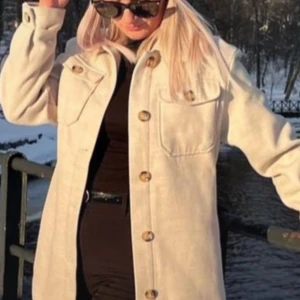 Beige jacka med knappar - Säljer en snygg beige jacka med stora knappar framtill. Den har en klassisk krage och två bröstfickor med knappar. Perfekt för höst och vår, och ger en stilren look. Passar både till vardags och lite finare tillfällen.