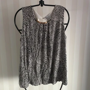 Svartvit mönstrad ärmlös topp från H&M - Säljer en snygg svartvit ärmlös topp från H&M med ett coolt mönster. Toppen har en metallring vid halsen och en liten öppning i ryggen. Perfekt för både vardag och fest! 🖤🤍