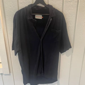 Mörkblå kortärmad skjorta från Revolution - Säljer en svart kortärmad skjorta från Revolution i storlek XL. Skjortan har en klassisk krage och en bröstficka. Perfekt för både vardag och fest!  Nypris: 699kr skick 8/10