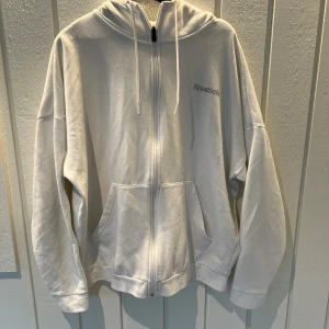 Vit hoodie från Reebok - Säljer en vit hoodie från Reebok i storlek L. Den har en dragkedja framtill och en snygg gul detalj längs ärmarna. Perfekt för både vardag och träning. Gjord av återvunnet material, skick 8/10