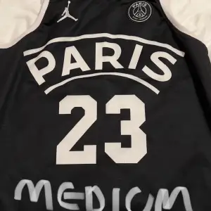 Säljer en svart Jordan linne med Paris-motiv och nummer 23. Tröjan har vita detaljer och är kortärmad. Perfekt för sportiga tillfällen eller som en cool vardagslook. Skön och stilren design!