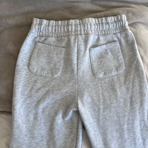 Grå mjukisbyxor med snörning - Superbekväma grå mjukisbyxor i bomull med elastisk midja och snörning. Perfekta för en chill dag hemma eller en snabb tur till affären. Byxorna har två fickor bak och två fram, vilket gör dem både praktiska och stiliga. Passar perfekt för höst och vintermys! Från lager 157