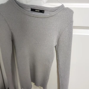 Glittrig grå tröja från Bik Bok - Säljer en superfin glittrig grå tröja från Bik Bok i storlek XS. Den är ribbad och har långa ärmar, perfekt för både vardag och fest. Tröjan är i nyskick. ✨