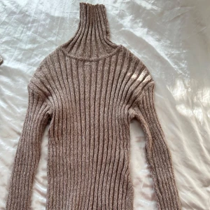 Beige ribbad polotröja - Säljer en supermysig beige polotröja med ribbat mönster. Perfekt för kyliga dagar med sin höga krage och långa ärmar. Tröjan är i ett mjukt och stretchigt material som sitter skönt på kroppen.✨
